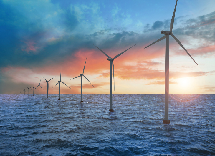 Havvindmøllepark med vindmøller mod en dramatisk orange og blå solnedgang.